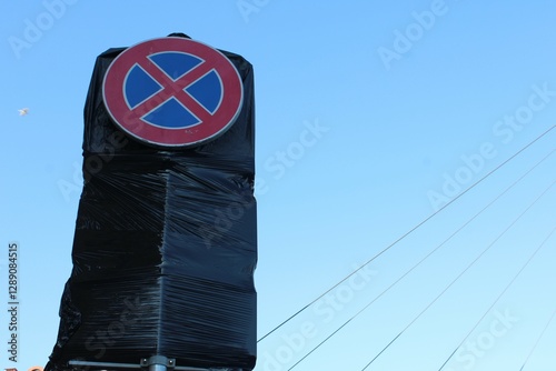 A no parking sign partially covered with black plastic wrap against a clear blue sky. A symbol of temporary traffic restrictions or road changes