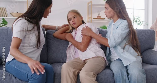 Worried mother, sister and grandmother gathering around unhappy teenage girl on couch, comforting her in difficult life situation with gentle words and supportive embraces in warm caring atmosphere.