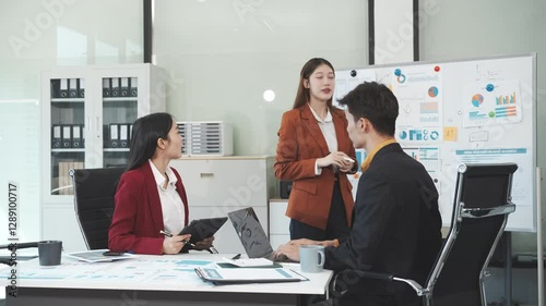 Three Asian business professionals gather in boardroom for annual meeting, discussing strategic goals, future projections while proposing ideas, engaging in decision-making for corporate growth.