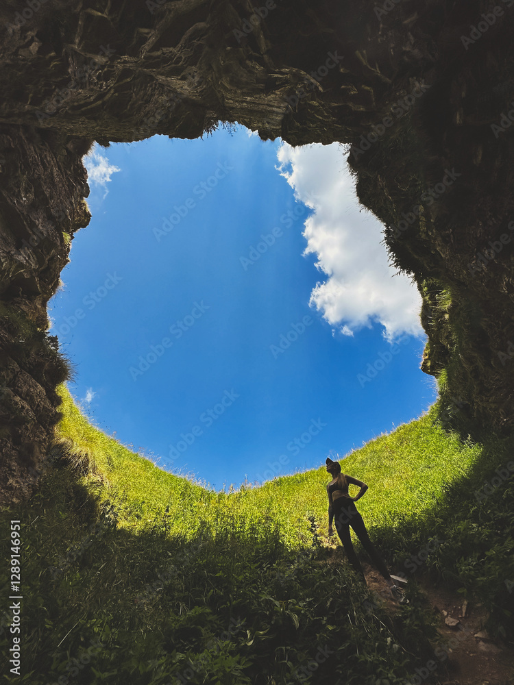 Woman Standing in Underground Cave with Hole to Outside