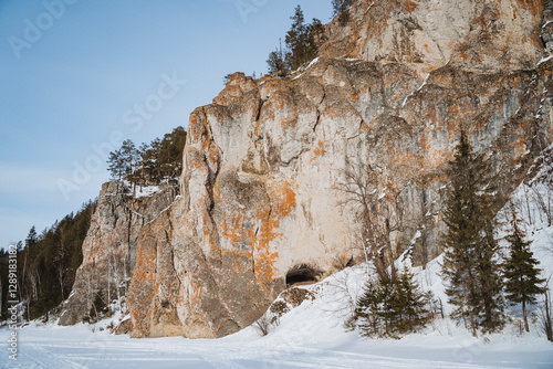 The snowcovered rock formation has inviting entrances, surrounded by tall evergreens, creating a serene winter landscape that evokes tranquility and adventure
