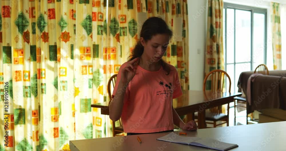 Studious woman focuses on notes performing sign language gestures. Diligent brunette recreates finger movements to be interpreter at table against window curtain in room