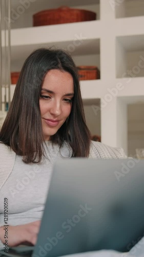 A young woman smiles while working from home on her laptop. She appears happy and productive