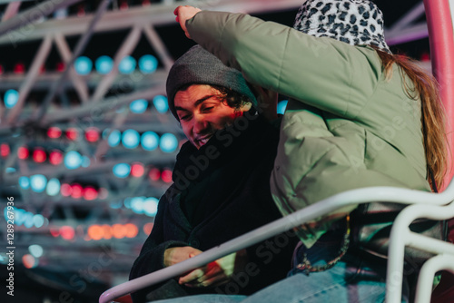 Young couple sitting on a ride at a carnival during nighttime, under vibrant lights, sharing a joyful moment. The image captures the excitement and togetherness of the fair atmosphere.