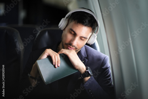 Handsome business man sleeping in airplane cabin during flight sitting near window.