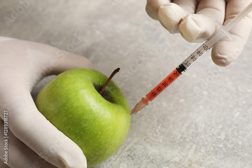 GMO concept. Scientist injecting something into green apple at grey table, closeup