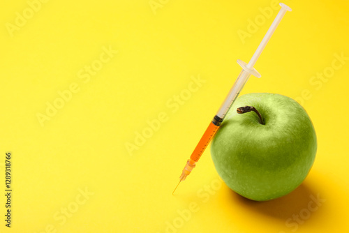 GMO concept. Green apple and syringe with liquid on yellow background, closeup. Space for text