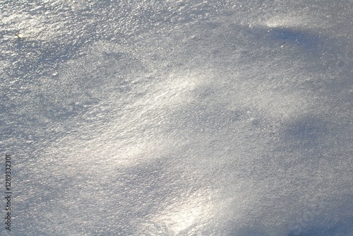Close-up of a snow-covered landscape glistening under sunlight. The smooth, icy texture reflects light, creating a mesmerizing winter scene with sparkling details