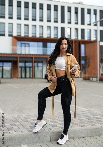 Model poses by modern building. A young woman stands in an urban setting, showcasing her stylish outfit against a backdrop of contemporary architecture.