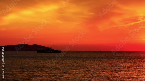 A serene sunset over the sea with a silhouette of a Princes islands and a ship underway. Sky painted in vibrant shades of orange and yellow, creating striking contrast with dark silhouettes. Istanbul,