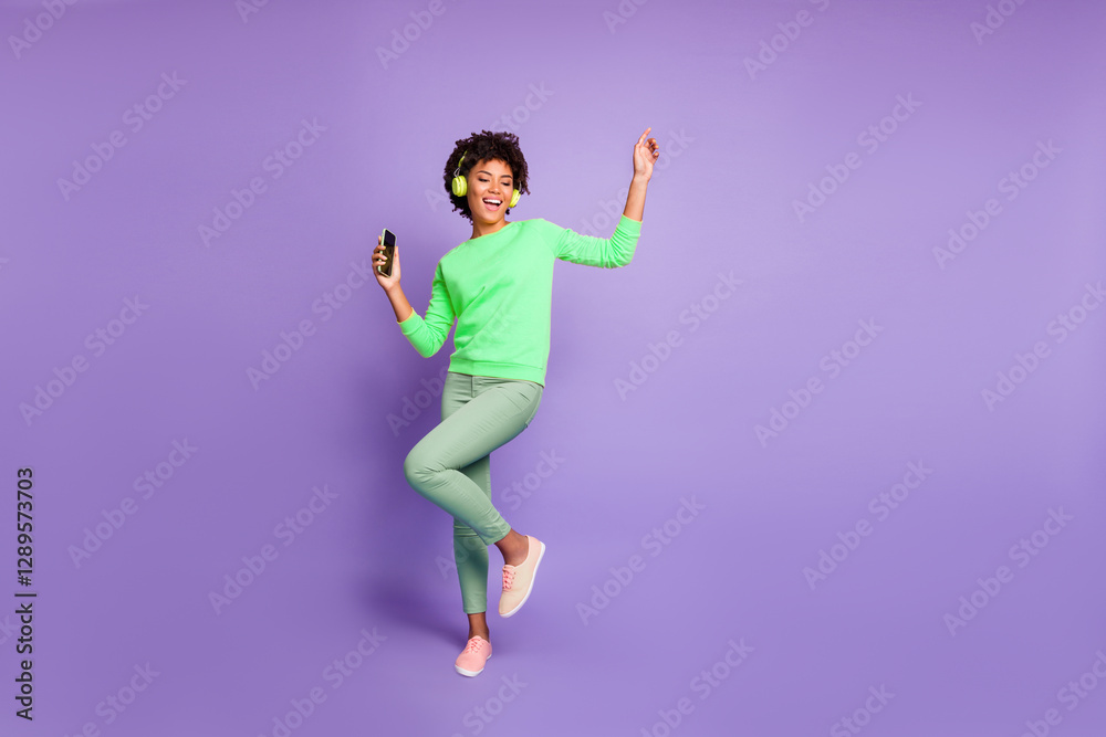 Full length body size photo of trendy stylish cute free girlfriend wearing green pants trousers yellow sweater footwear in headphones listening to music dancing isolated violet pastel color background Full length body size photo of trendy stylish cute free girlfriend wearing green pants trousers yellow sweater footwear in headphones listening to music dancing isolated violet pastel color background