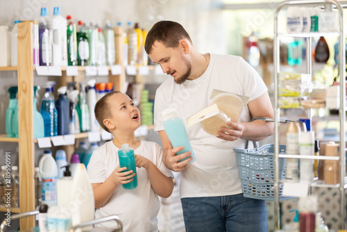 Young man with his son buyers chooses shampoo or shower gel and body washcloth in household chemicals store
