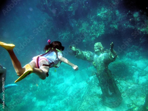 Quadro su tela Underwater shot of a young girl snorkeling to the Christ of the Abyss Statue off Key Largo Florida Gulf of Mexico with fish swimming around and plant life growing