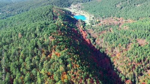 Şirinyazı Pond in Mengen, Bolu during autumn. Vibrant colors of the season are on full display with green pines and shades of red and yellow leaves. Dense forest surrounding the pond adds depth and te
