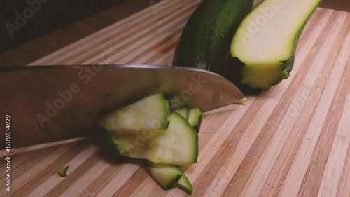 Cutting long green courgettes in slow motion with a knife on a wooden board. Chopped courgette. Chef slice zucchini with a closeview. Slow motion cooking video. Fresh italian salad with courgette. 