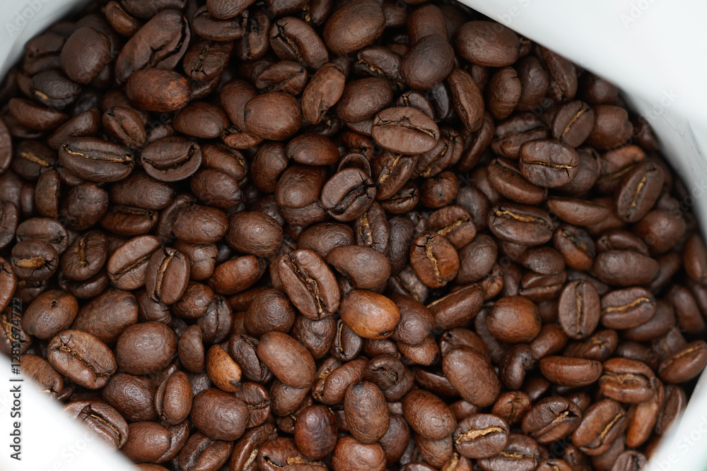 Obraz premium Dive into the rich, aromatic world of freshly roasted coffee beans with this captivating stock photo. Featuring a close-up view of dark, glossy coffee beans nestled in a pristine white container.