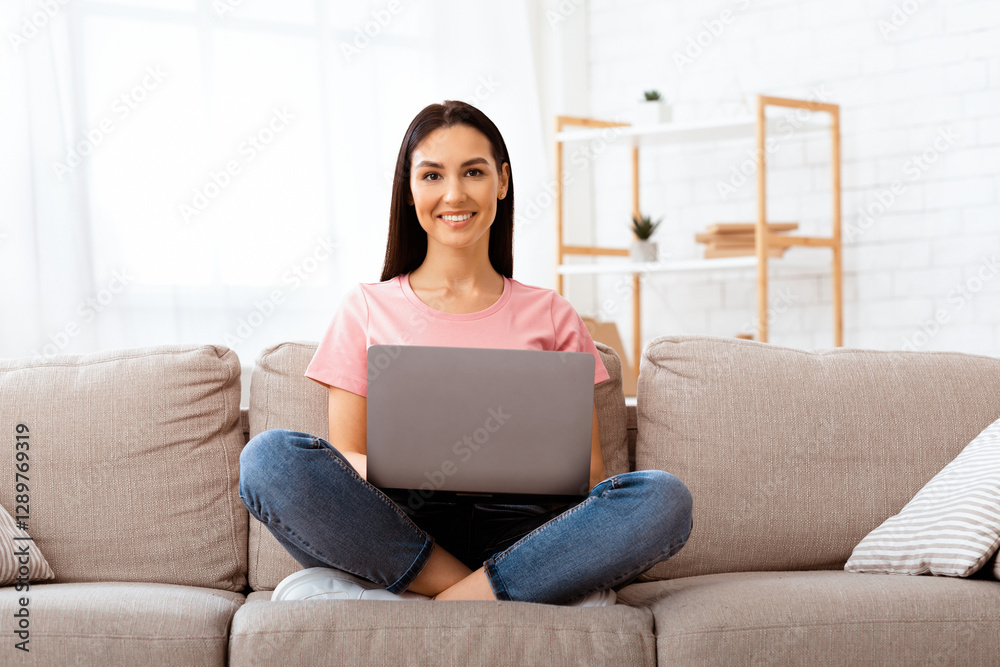 Carefree Time At Home. Beautiful young woman working on laptop and smiling while sitting on the couch at home Carefree Time At Home. Beautiful young woman working on laptop and smiling while sitting on the couch at home