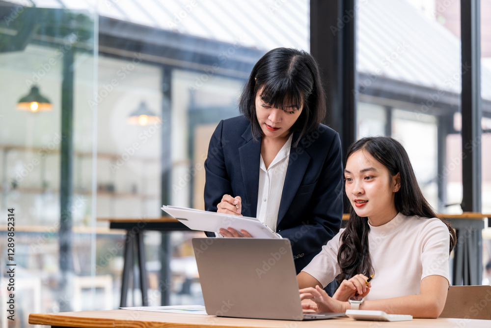 Two women are sitting at a table with a laptop open in front of them Two women are sitting at a table with a laptop open in front of them