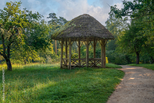 View of the ancient wooden gazebo in the apple orchard in the Mikhailovskoye Estate of the Pushkin Museum-Reserve on a sunny summer day, Pushkinskiye Gory, Pskov region, Russia photo