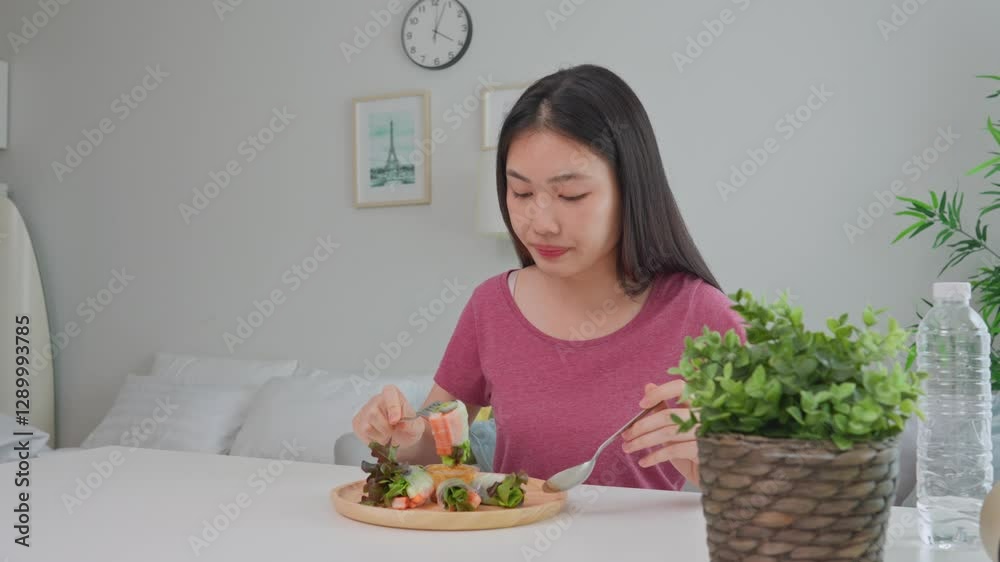 Asian young woman eating vietnamese spring rolls in living room at home. Asian young woman eating vietnamese spring rolls in living room at home.