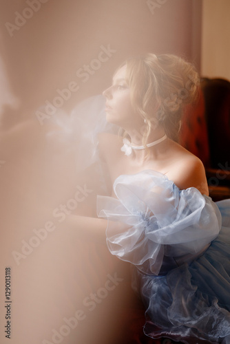 Graceful young woman in elegant light blue dress posing in the interior of an old manor. Fairytale or historical theme concept for a book cover or a classical music album.