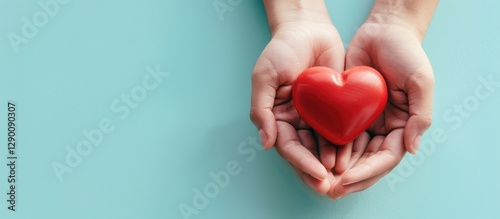Hands holding a vibrant red heart on a soft light blue background with a clean copy space area to the left.