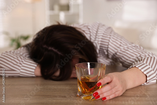 Alcohol addiction. Woman with glass of whiskey at wooden table indoors, selective focus photo