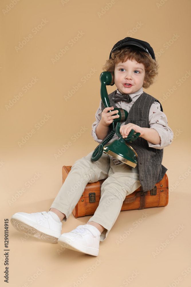 Cute little boy with old telephone and suitcase on beige background