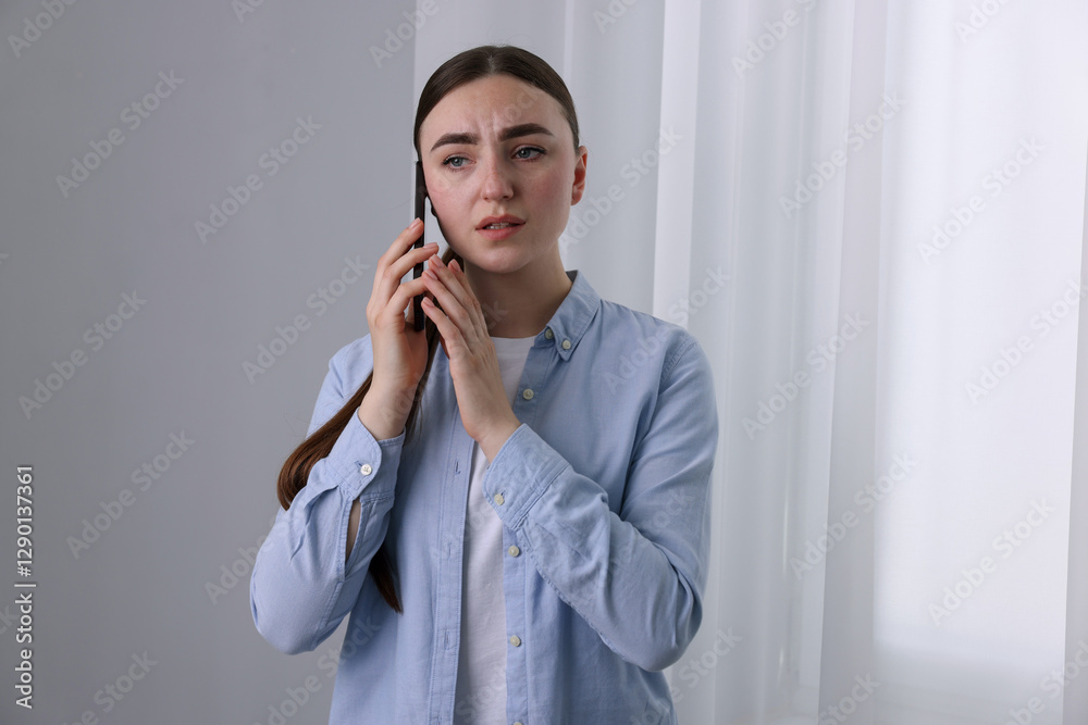 Stressed woman calling hotline for mental health help near window at home Stressed woman calling hotline for mental health help near window at home