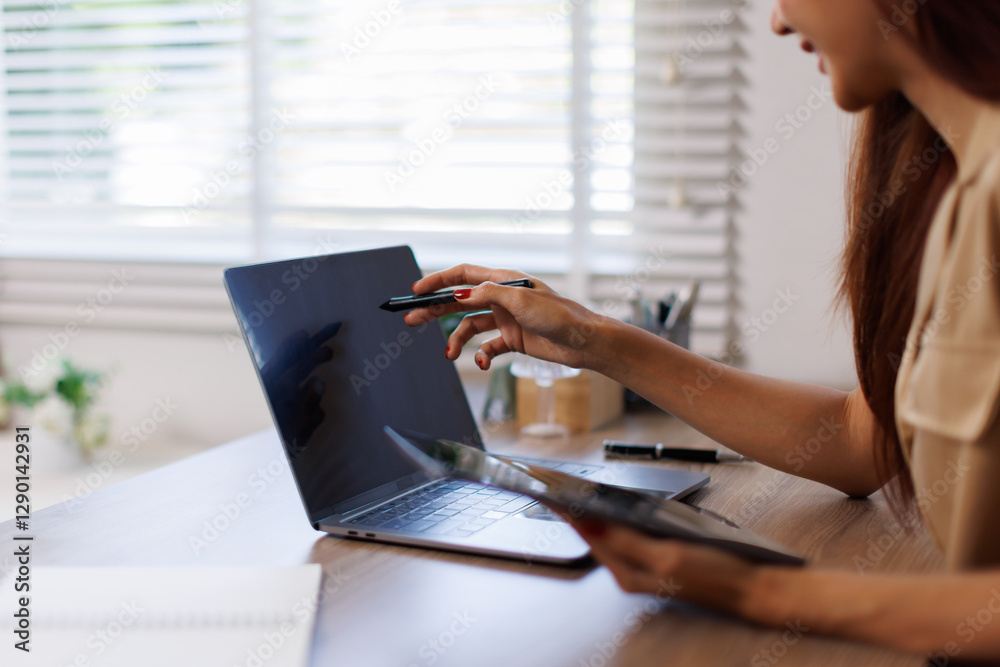 Fototapeta premium Portrait of a smiling young Asian business woman work on her desk in a large modern office working online Business Analytics with a digital tablet