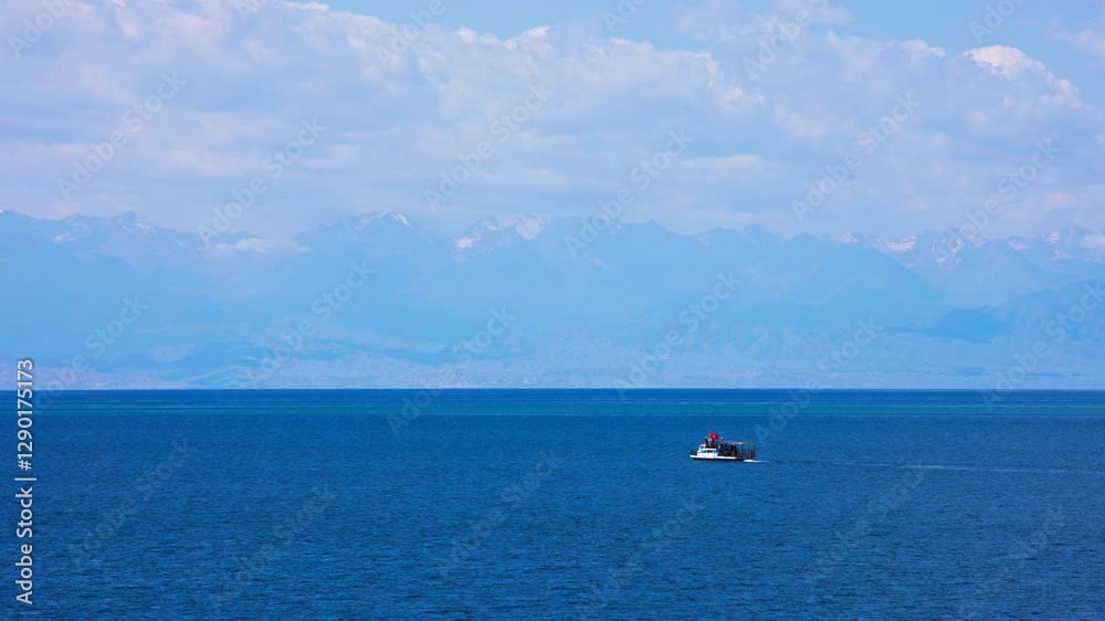 Small white passenger cruise boat on Lake Issyk-Kul, Kyrgyzstan, with stunning snow-capped mountains in the background. The calm blue water and clear sky create a peaceful and scenic landscape. Small white passenger cruise boat on Lake Issyk-Kul, Kyrgyzstan, with stunning snow-capped mountains in the background. The calm blue water and clear sky create a peaceful and scenic landscape.
