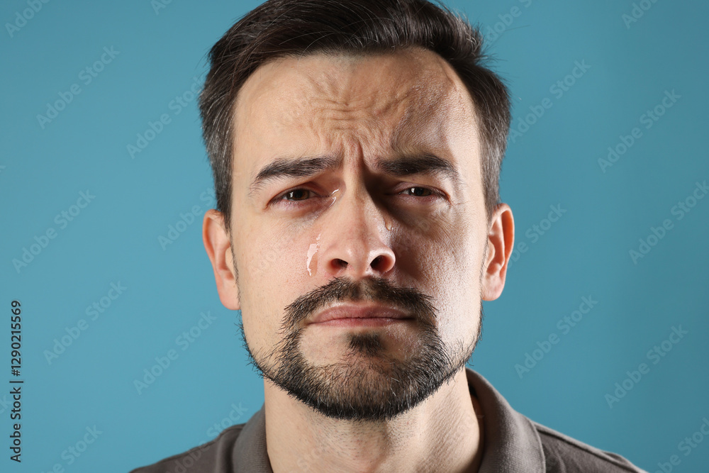 Fototapeta premium Sad man crying on light blue background, closeup