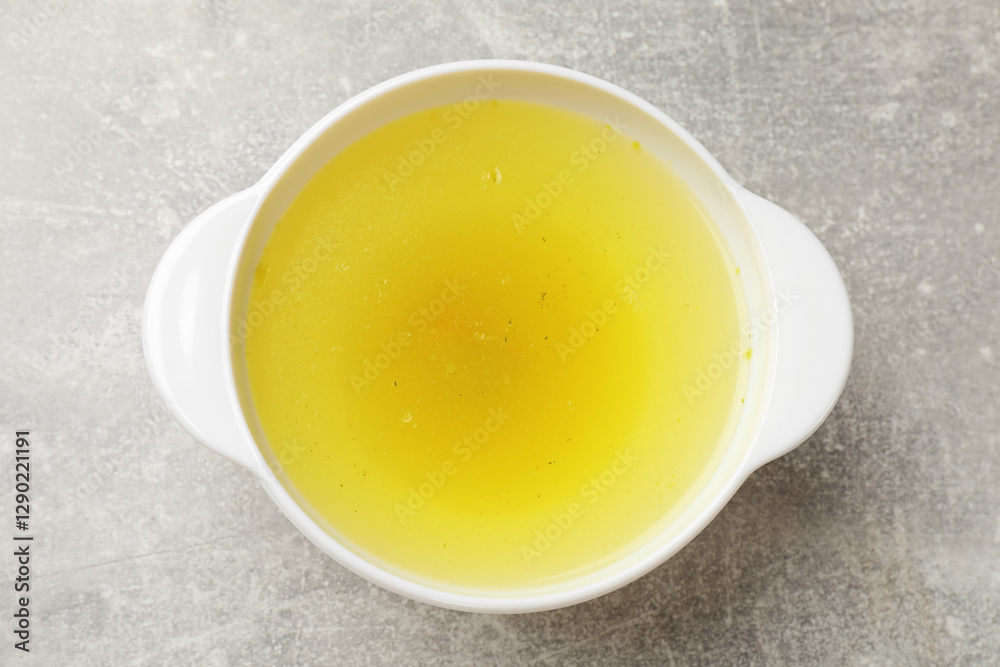 Tasty chicken bouillon in bowl on grey table, top view Tasty chicken bouillon in bowl on grey table, top view