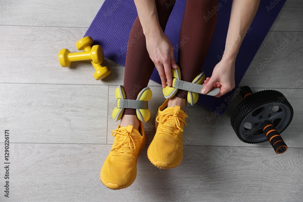 Fototapeta premium Woman putting on ankle weights and gym equipment indoors, top view