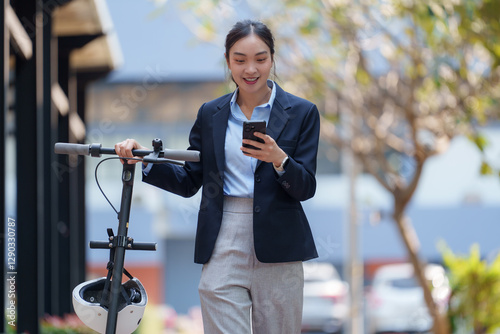 Young businesswoman is using her smartphone while holding an electric scooter, showcasing modern commuting and technology in an urban environment