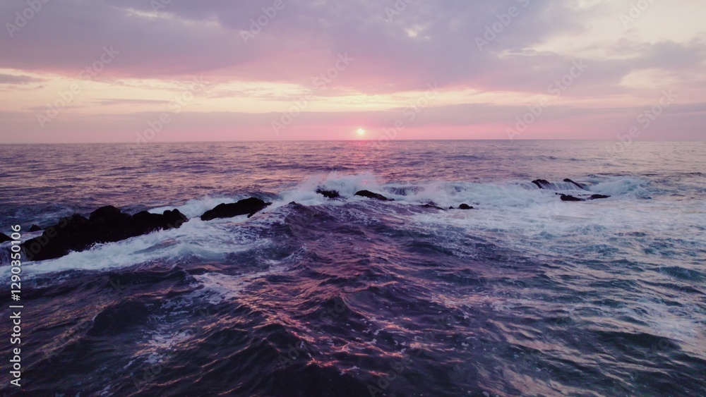 Obraz premium A bird's-eye view of the sea at sunset. Foam waves wash the stone reefs on the shore. Drone video