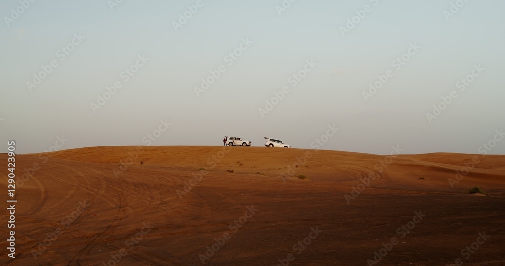 Two men walk around cars with open trunks standing on top of a sand dune in the desert Two men walk around cars with open trunks standing on top of a sand dune in the desert
