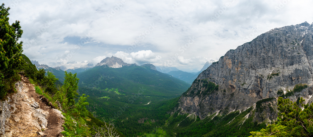 Breathtaking view of forests, mountains, and valleys in the Italian Dolomites (Dolomiti, Dolomiten). Captured from a scenic trail along a rocky ledge. Stunning alpine nature