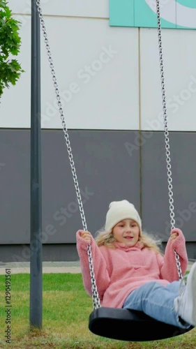 Young female in pink hoodie enjoying swing at playground during sunny summer day with joyful smile and vibrant colors