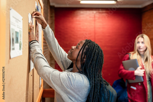 Foto Young student putting up a notice on university bulletin board