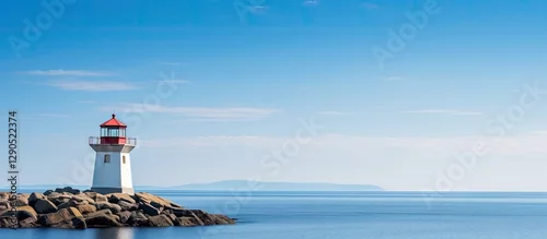 Obraz  z motywem Lighthouse with red top on rocky shore under clear blue sky calm sea in tranquil coastal scenery with distant mountains in background