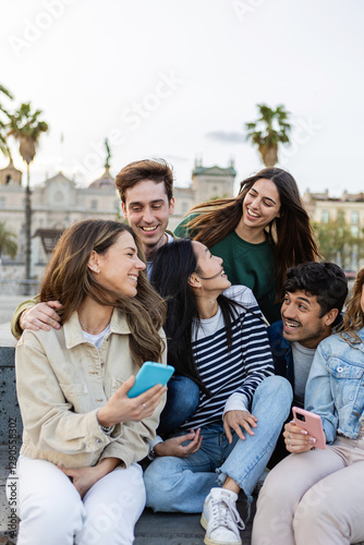 Vertical shot of young group of happy friends laughing while using mobile phones at city street. Friendship lifestyle and technology concept