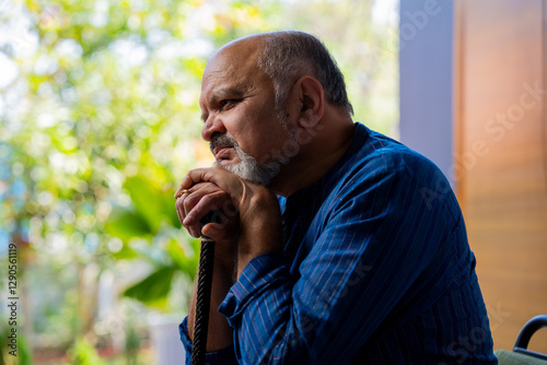 Old Indian man in kurta holding walking stick, sitting alone on sofa with helpless expression