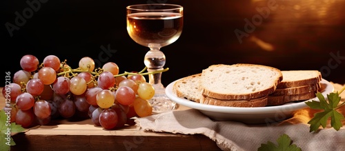 Grapes of various colors alongside a glass of dark wine and sliced unleavened bread on a rustic wooden surface with soft warm lighting. photo