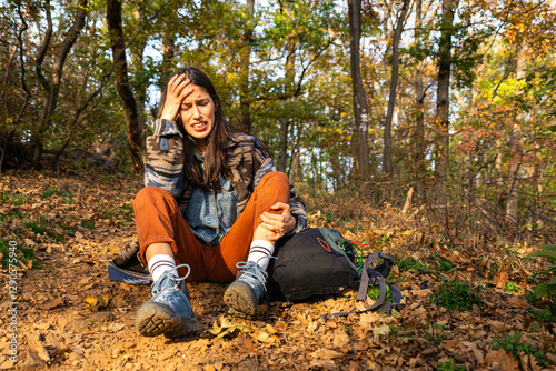 Obraz na płótnie Hiker woman sitting on a trail, clutching her leg in pain after an injury, with