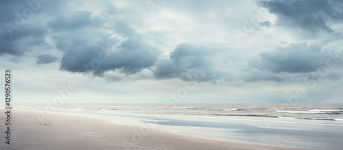 Serene beach landscape with grey clouds above, gentle waves lapping on sandy shore, soft muted tones of blue and grey creating a tranquil atmosphere.