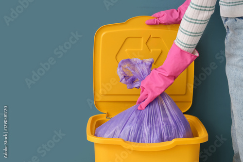 Woman taking garbage bag from trash bin near blue wall, closeup