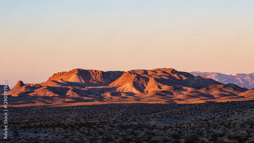 Naklejka premium A stunning view of a desert mountain range at dawn, showcasing warm colors as the sun rises, creating a dramatic contrast with the arid landscape.