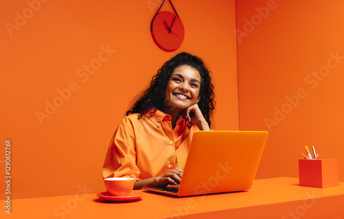 Female working from home on laptop, smiling in monochromatic minimalist office setup photo