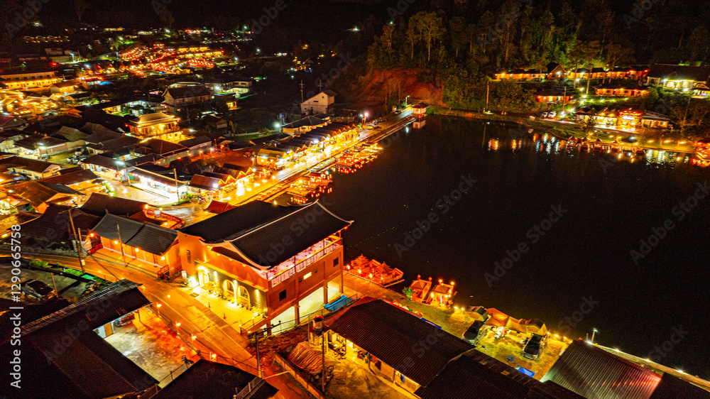 Fototapeta premium Baan Rak Thai Village at sunset reflections of houses and restaurants along the lake in Chinese-style architecture with colorful lights line the water. a popular tourist attraction in Mae Hong Son